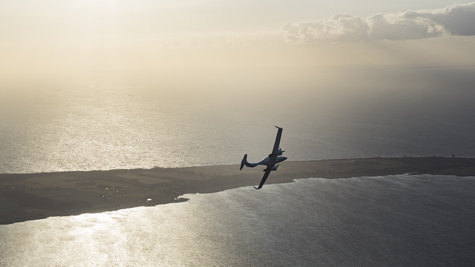 Trainingsflugzeug fliegt über Küstenabschnitt bei Sonnenuntergang.