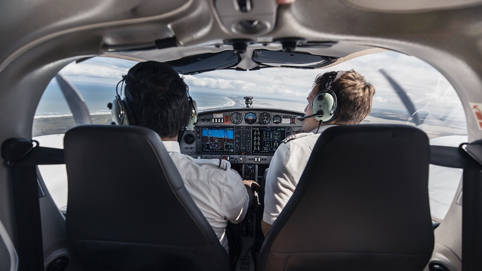 Flugschüler:in und Fluglehrer:in fliegen in einem Schulungsflugzeug über eine Küstenlandschaft