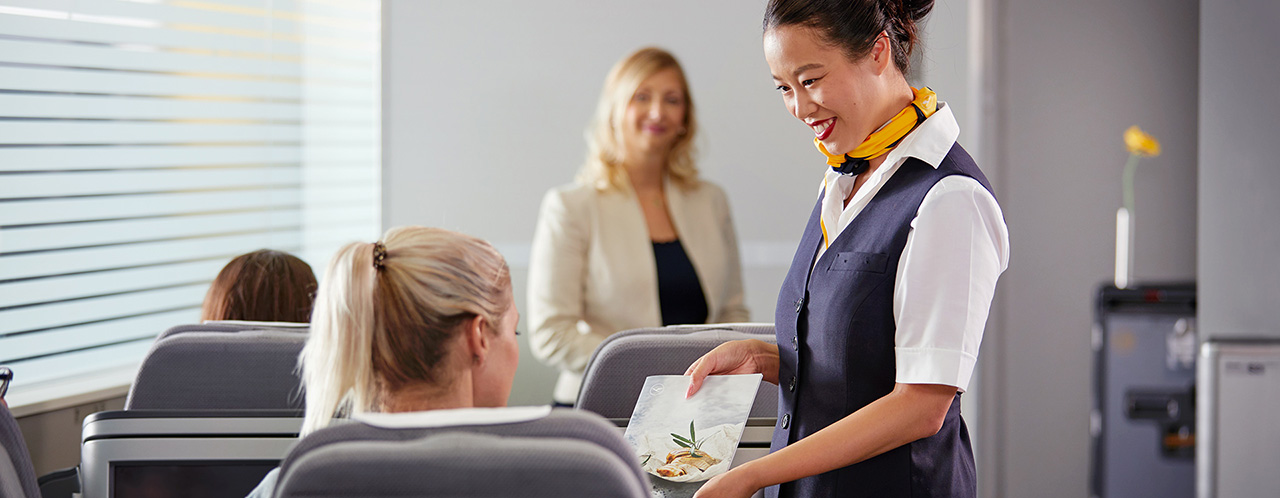 A flight attendant offers the menu to a passenger in a training situation.