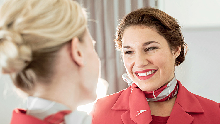 Two smiling flight attendants of Austrian Airlines wear uniforms and scarves