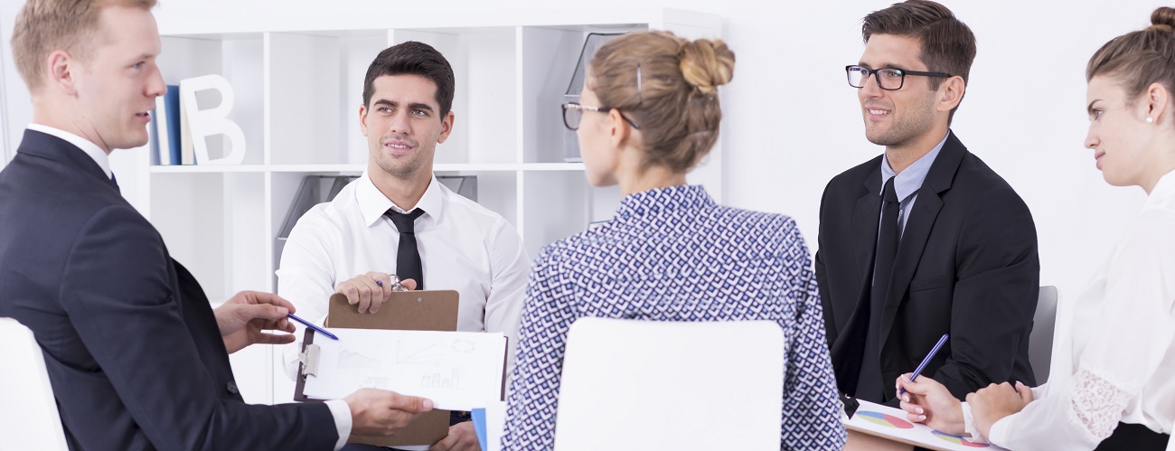 Fünf Personen in Business Kleidung sitzen an einem Tisch und halten ein Meeting ab.