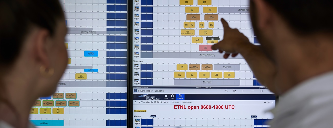 2 Personen sitzen in einem Flugsimulator für ein Schulungsflugzeug. Außerhalb befindet sich ein Display, auf dem eine Startbahn angezeigt wird.