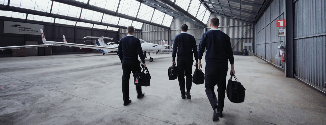  Three student pilots walk towards a training aircraft parked in a hangar.