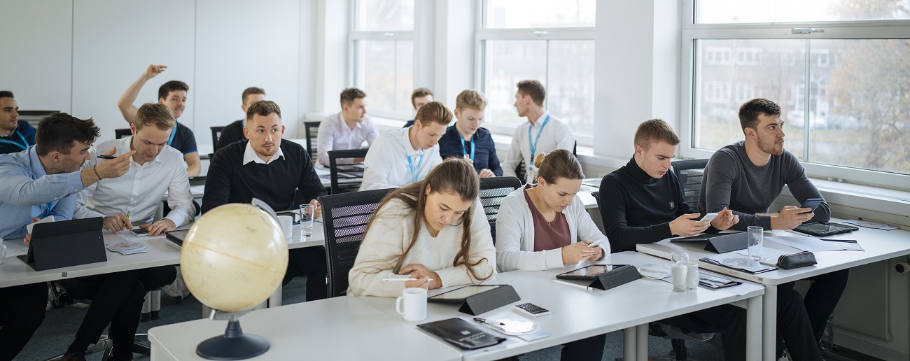 In einem Klassenzimmer sitzen einige Personen und arbeiten an Tablets oder diskutieren.