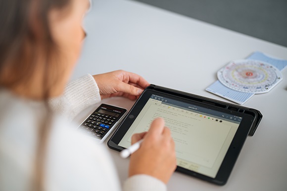Eine Person sitzt an einem Tisch und arbeitet parallel am Taschenrechner und Laptop und informiert sich über die Kosten einer Pilotenausbildung.