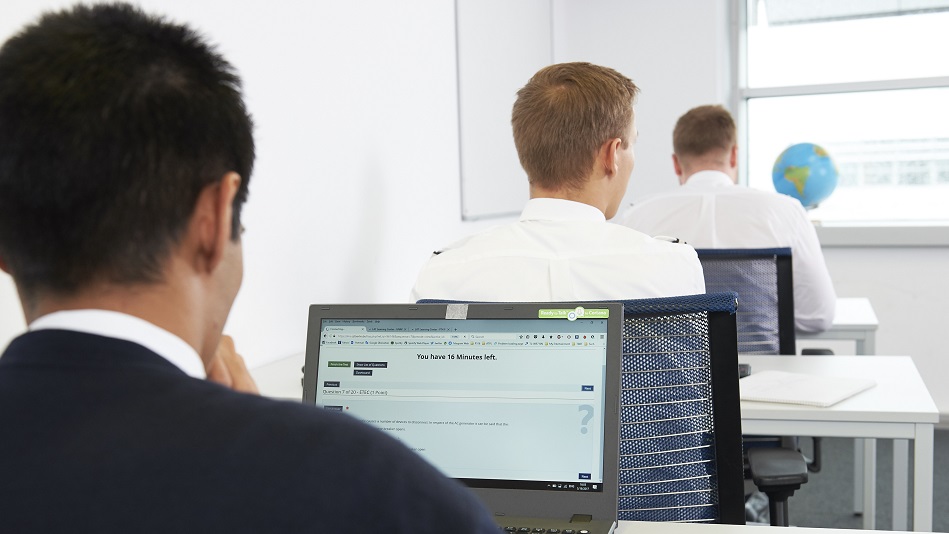 Drei Personen sitzen hintereinander an Tischen vor Laptops und lösen Aufgaben