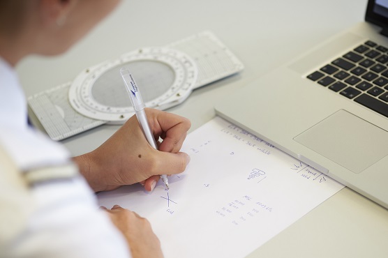  A student pilot sits in front of an open laptop and makes notes on a piece of paper.