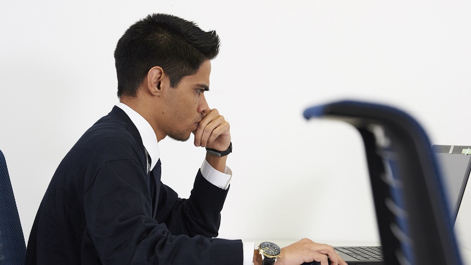 A person sits at a table and writes on the application for ab initio pilot training on a laptop