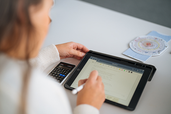 A person sits at a laptop and holds a calculator in one hand.