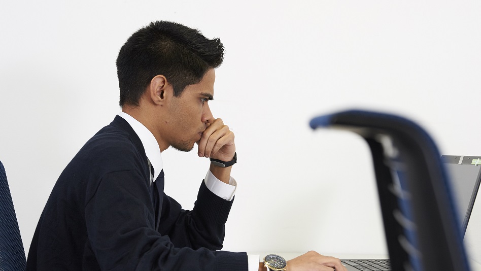 Eine Person sitzt an einem Schreibtisch und schreibt eine Bewerbung an einem Laptop.