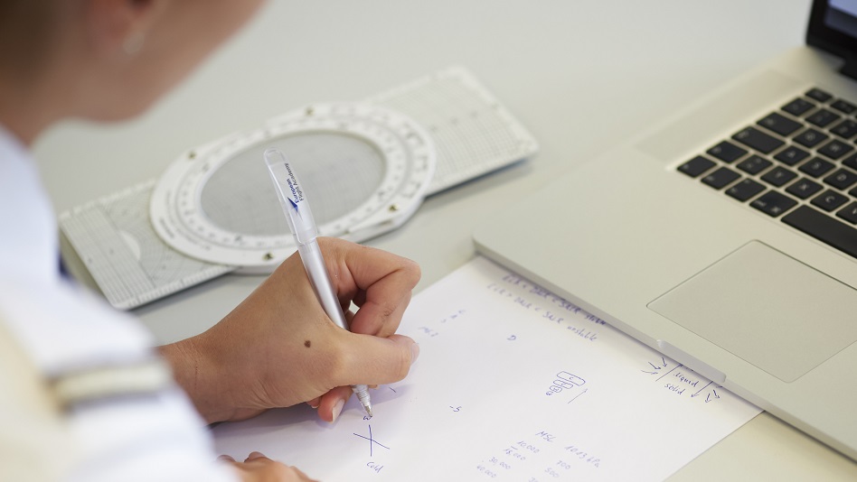 A person sits in front of a laptop and takes notes.