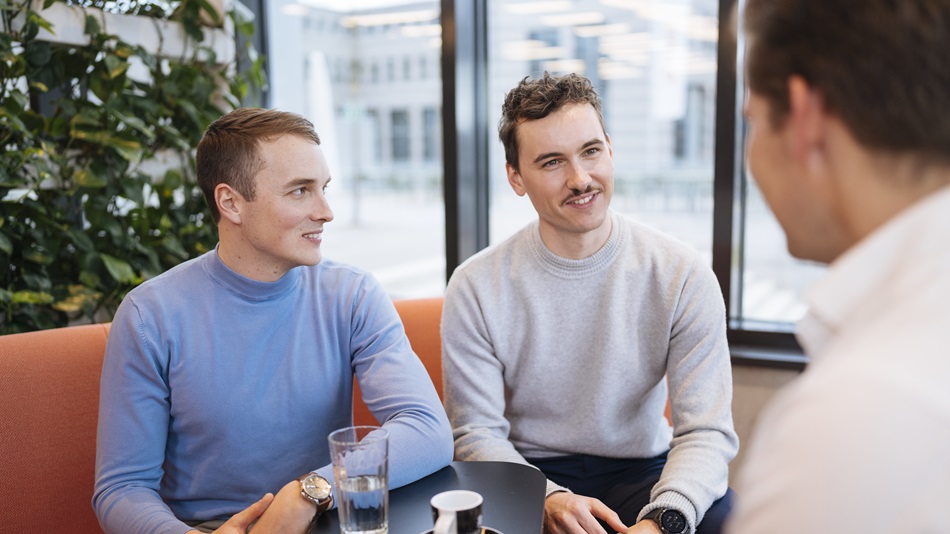 Three people are sitting in a cafeteria and talking to each other.
