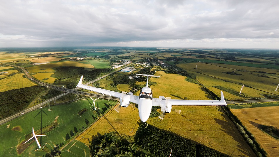 Training aircraft flies over fields and wind turbines.