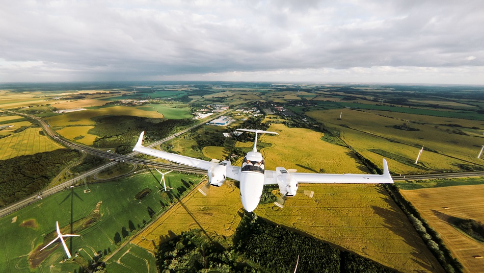 Trainingsflugzeug fliegt über Felder und Windräder.