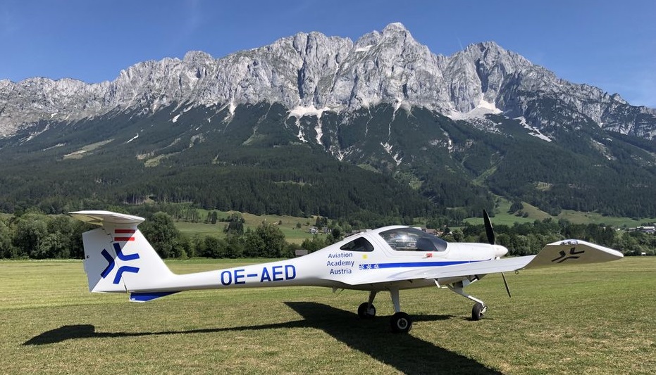 Ein Schulungsflugzeug steht auf der Wiese vor einer Bergkulisse.