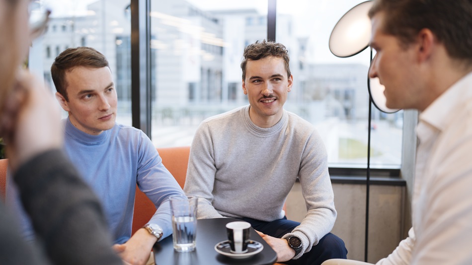 Eine Person sitzt an einem Tisch und arbeitet am Laptop, daneben steht ein Stapel Bücher.