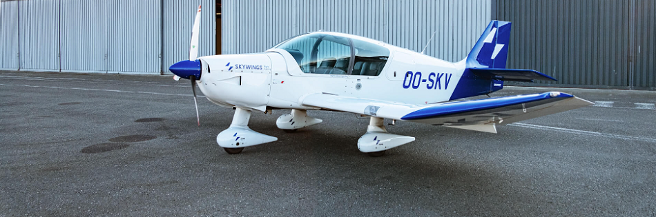 A training aircraft is parked in front of a hangar.