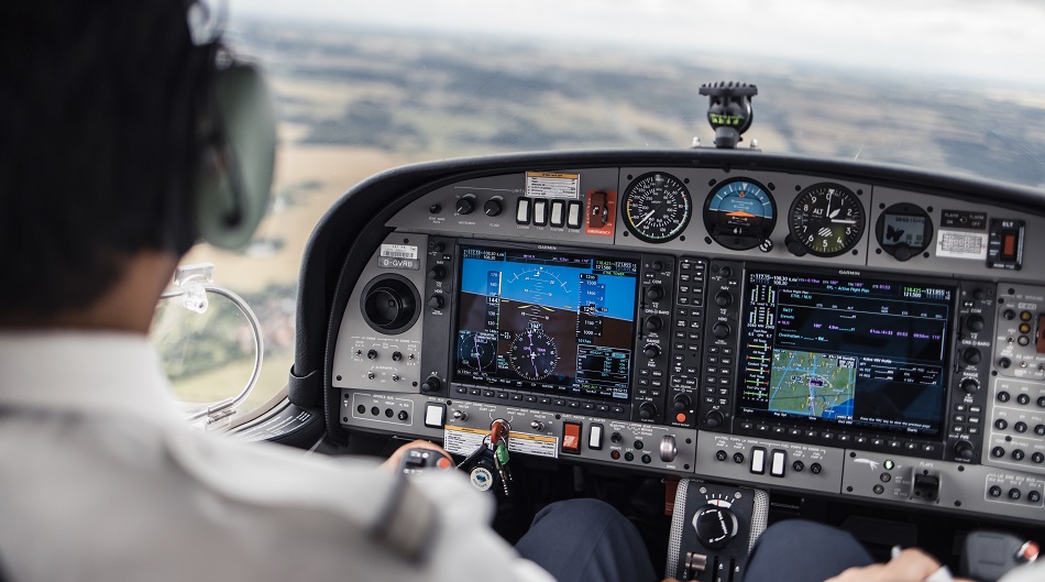 Eine Person sitzt in einem Schulungsflugzeugt und steuert das Flugzeug über eine Landschaft.