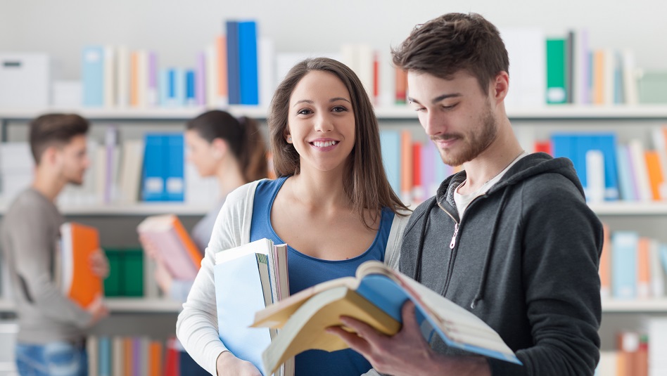 Zwei Personen stehen mit Büchern in der Hand in einer Bibliothek.
