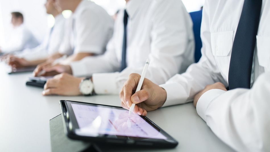 Mehrere Flugschüler:innen sitzen an einem Tisch, im Vordergrund arbeitet eine Flugschüler:in an einem Tablet.