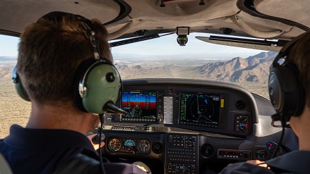 Zwei Personen sitzen im Cockpit eines Schulungsflugzeuges und steuern das Flugzeug über die Wüste Arizonas